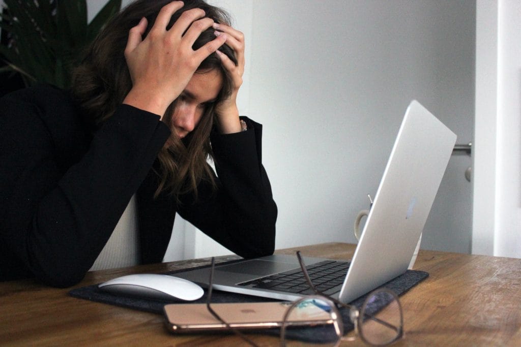 Woman with head in hands looking at laptop to represent how to deal with feeling overwhelmed